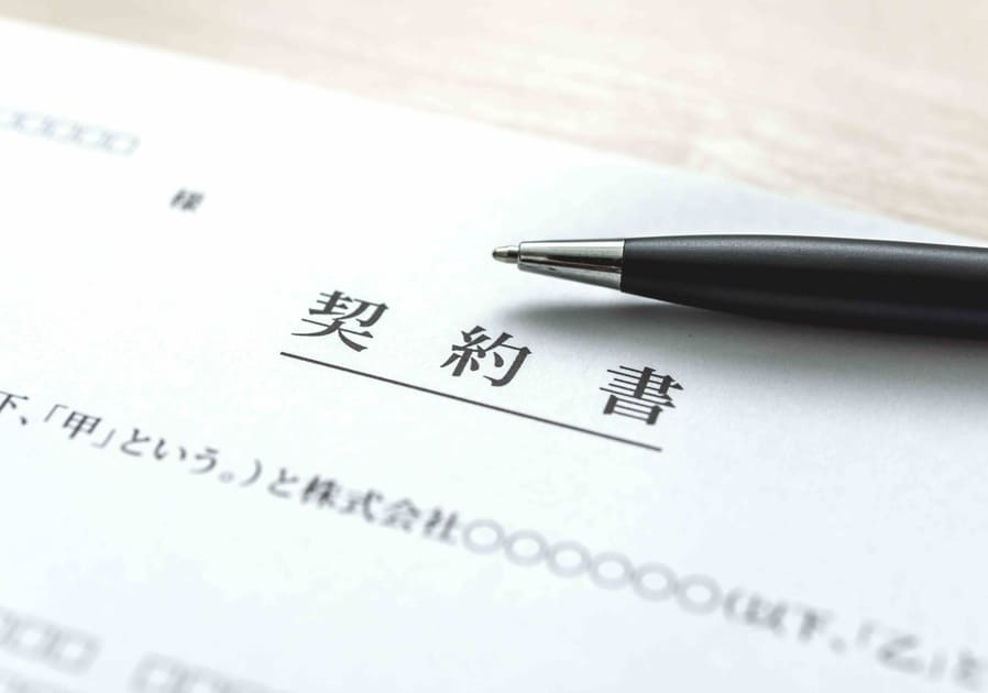 「契約書」の文字が記載された書類と、隣に置かれたボールペンのクローズアップ。